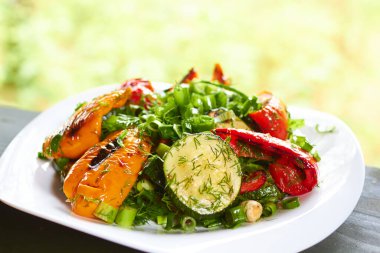 Izgara tatlı biber, kabak, yeşil soğan ve bitkilerle dolu bir yemek.