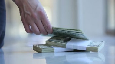 Kadın elleri dolar sayıyor ve masanın üstüne koyuyor.