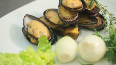 Beyaz tabakta midye, sarımsak, soğan ve salata yapraklı lezzetli gurme yemeği.
