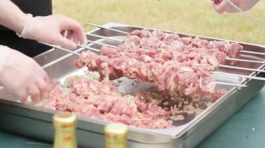 İnsanlar şişlerin üzerine taze et parçaları koyarlar. 