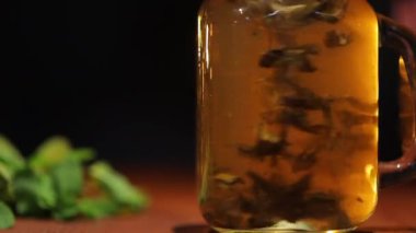 Cam kavanozda taze siyah çay ve ahşap masa üzerinde nane yaprakları.