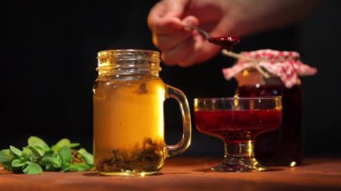 El biraz ahududu reçeli ekle cam kavanozda taze siyah çay ve ahşap masa üzerinde nane yaprakları olsun.