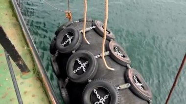 Büyük siyah şişirilebilir demirleme çamurluğu halatla sarkıtılmış.