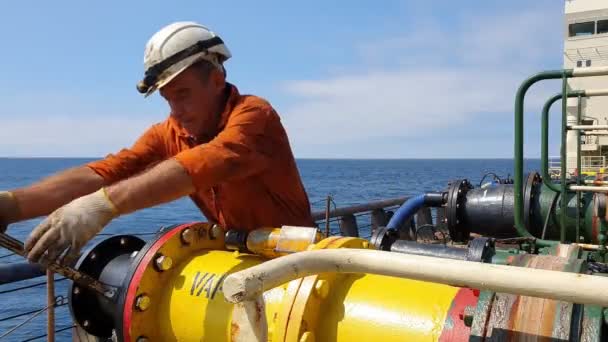 Pumpman in orange jumpsuit with helmet unscrews pipe — Stock Video