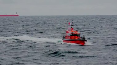 Parlak pilot teknesi liman yollarında gri deniz suyu boyunca yol alır.