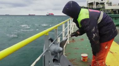 Gemi işçisi petrol tankeri güvertesinde tırabzanları beyaza boyuyor.