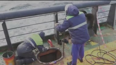 İşçiler petrol tankeri güvertesindeki kargo tankının kapağını değiştiriyor.