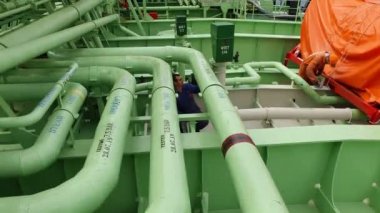 Tanker mürettebatı açık yeşil manzaralı boruları boyuyor.