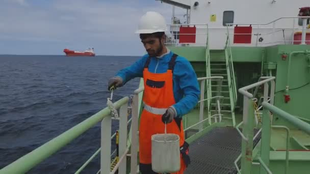 Matroos houdt emmer en schildert leuningen tegen kalme zee — Stockvideo