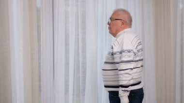 Beyaz çizgili süveter giyen yaşlı bir adam pencereye geliyor.