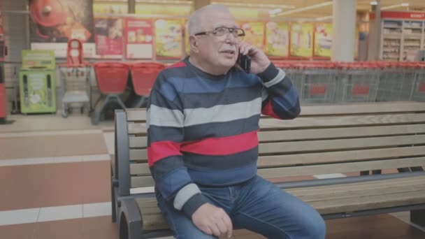 Uomo anziano in occhiali e maglione a righe parla al telefono — Video Stock