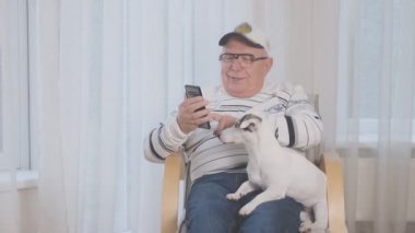 Gözlüklü emekli, sevimli köpeği okşuyor ve telefonda konuşuyor.