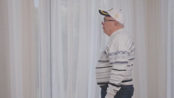 Старший человек в шапке и очках приходит к пластиковому окну — стоковое видео