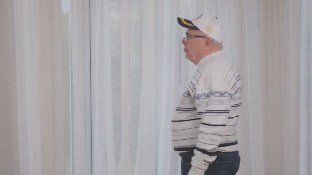 Senior man wearing cap and glasses comes to plastic window — Stock Footage Senior man wearing cap and glasses comes to plastic window Royalty Free Stock Footage