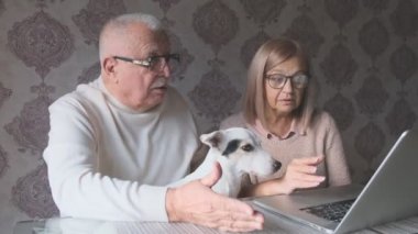 Yaşlı adam komik bir köpek tutuyor. Sarışın karısının yanında oturuyor.