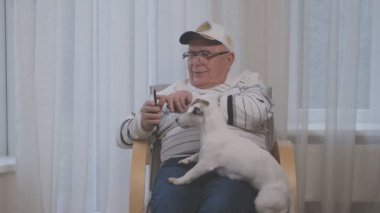 Gülümseyen yaşlı adam akıllı telefon ekranını beyaz köpeğe gösteriyor