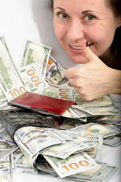 脸上的中年女子微笑着 手里拿着一双幸运的拇指 旁边躺着一大笔钱 百美元的美国钞票钱包红色和钱包黑色 — 图库照片