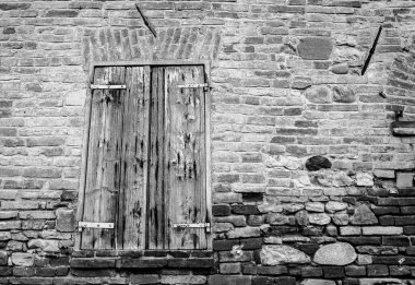 Kırsal evin pencere panjuru, tuğla duvar ve antik taşlarla kaplı. Paslanmış demir menteşeleri ve çatlak boyası olan hasarlı bir pencere..