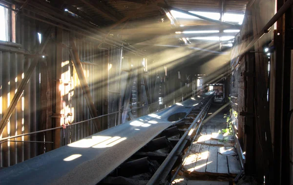 Die Sonnenstrahlen bahnen sich ihren Weg durch Löcher in Wänden und Decke eines alten Aufzugs zum Förderband Stockbild