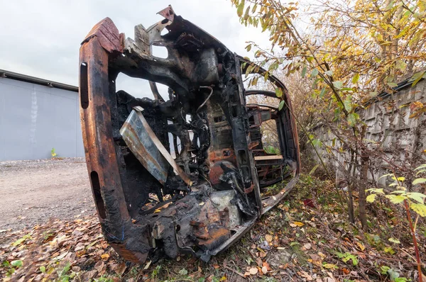 Rusty burned-out SUV on its side. Near the concrete fence on the background of trees and fallen leaves — Stock Photo, Image