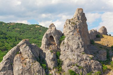 Arka planda bir grotto alışılmadık bir biçimle Hills ormanlar ve bulutlu bir gökyüzü ile dağıdır. Delikli Kaya kaya, Kırım Yarımadası