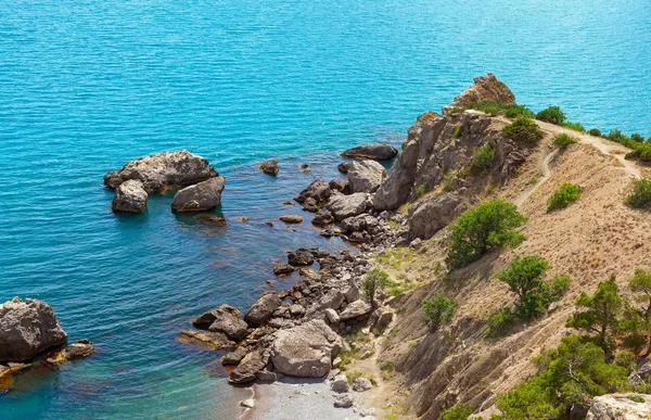 Orilla rocosa con piedras grandes en el agua de un color azul brillante — Foto de Stock