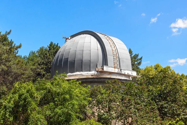 Closed dome of the old telescope in the observatory is among the crowns of trees.