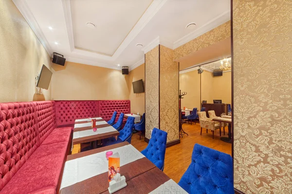 Moskau - September 2014: das Innere des Café Grill Bar na medovoy. großes weinrotes Ecksofa mit hoher Rückenlehne im Zimmer mit Tischen und blauen Stühlen — Stockfoto