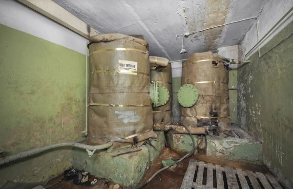 Large tanks with a supply of drinking water for autonomous existence in the underground shelter. An abandoned old shelter with a sign in Russian \