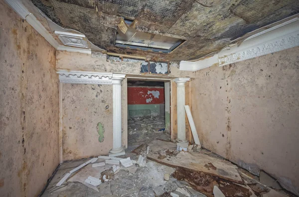 Room in an old abandoned Soviet shelter with decorative antique columns and garbage on the floor. Dampened suspended ceiling with mold.