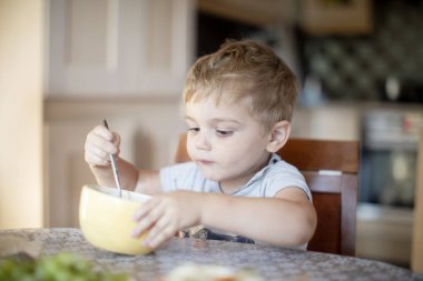 Sarı saçlı çocuk mutfakta yemek yiyor.