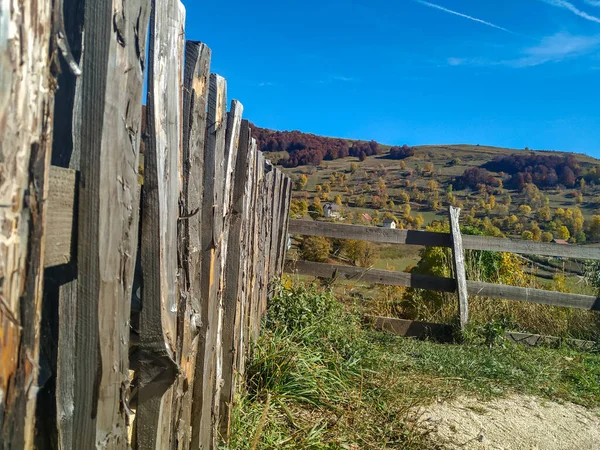 Alter, rustikaler Zaun an der Seite mit grünen Wiesen und kleinen Berghäusern im Hintergrund an einem sonnigen Herbsttag und klarem blauen Himmel — Stockfoto