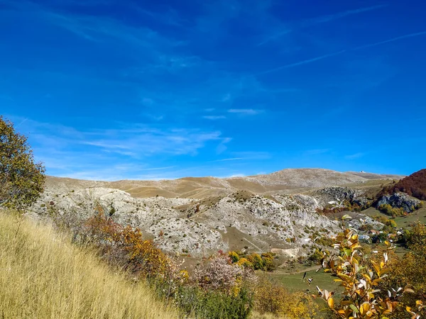 Rocky montanha deserta Bjelasnica em alpes DInaric durante o outono com grama amarela, árvores e rochas cinzentas. Pequena aldeia com casas . — Fotografia de Stock