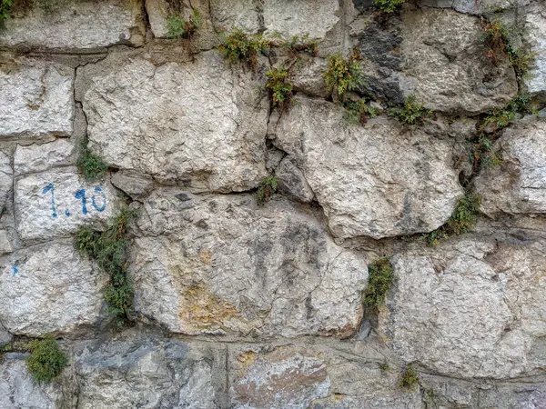 Alte riesige Steinfelsen, die eine Mauer als traditionelles Mauerwerk mit Gras und anderen grünen Pflanzen bilden, die mit Zeichen des Alters und des Verfalls hervorstechen — Stockfoto