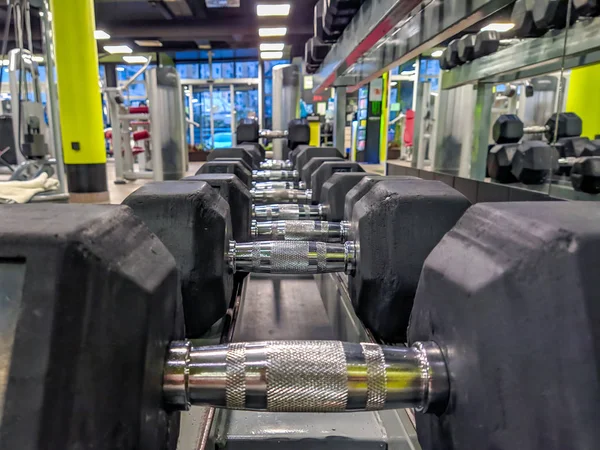 Black heavy dumbbells stacked in a row and organized in a well equipped and modern gym interior for recreational and healthy lifestyle exercise — Stock Photo, Image