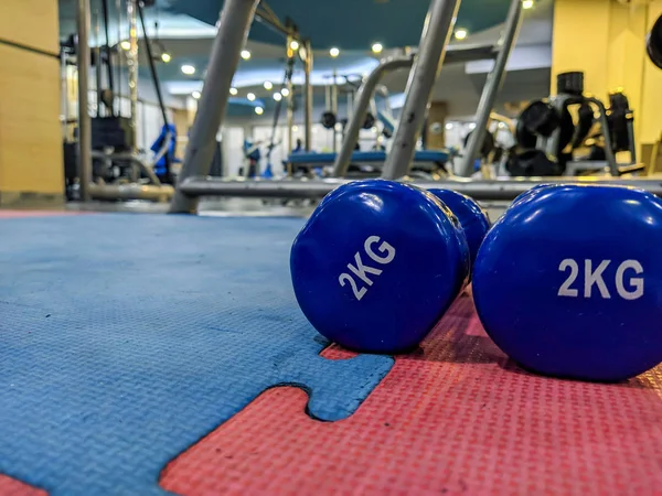 Νέο Έτος ανάλυση για να ξεκινήσετε τη μετάβαση στο γυμναστήριο με closeup των μικρών 2 κιλών αλτήρες σε μπλε χρώμα σε λαστιχένιο έδαφος σε ένα καλά εξοπλισμένο εσωτερικό γυμναστήριο — Φωτογραφία Αρχείου