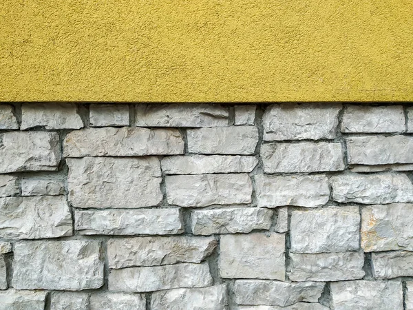 Cool wallpaper background with one side in the smooth wall in yellow color and other side made of stone rock bricks on the wall building in uneven pattern and rough texture