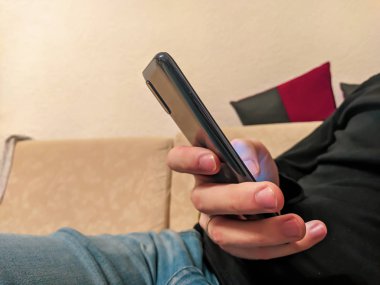 Akıllı telefon tutan bir adam, kanepede otururken telefonla yazı yazıyor.