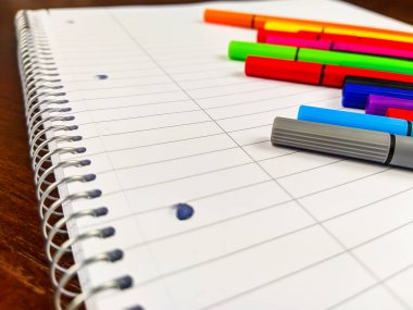 Not defteri spirallerinin ve renkli kalemlerin kapandığı boş beyaz bir defterin üzerinde satırlar, okulda veya iş yerinde not almak için kullanılır.