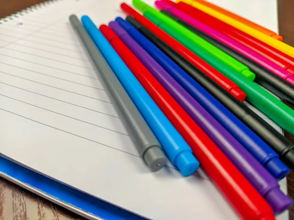Primer plano de las plumas de colores que se encuentran en un cuaderno blanco vacío para escribir notas como un equipo o suministros para la escuela o el estudio — Foto de Stock