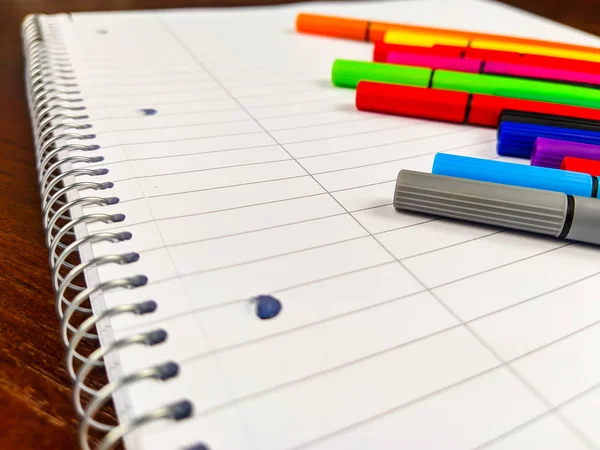 Primer plano de cuaderno espiral y plumas de colores que yacen en un cuaderno blanco vacío con líneas, utilizado para la toma de notas en la escuela, mientras estudia o en los negocios — Foto de Stock