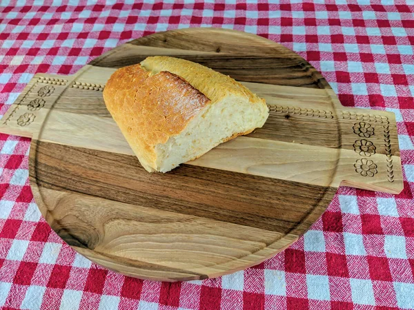 Top view of a beautiful homemade bread in golden color laying on wooden cutting board and colorful red tablecloth, healthy and appetizing meal — Stock Photo, Image