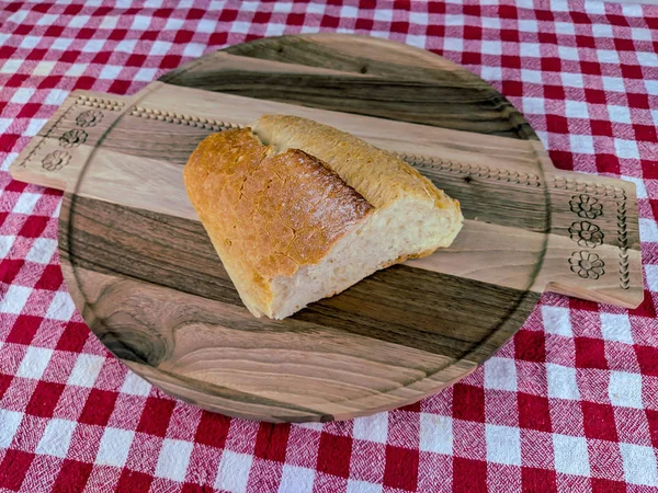 Top view of a beautiful homemade bread in golden color laying on wooden cutting board and colorful red tablecloth, bread that is sliced up. — Stock Photo, Image