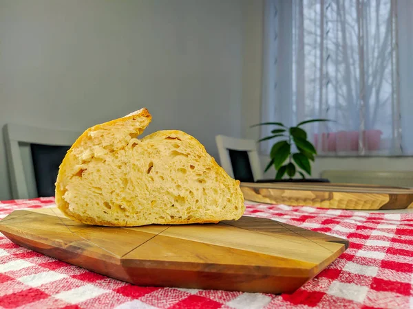 Side view of a delicious homemade bread on wooden cutting board and colorful tablecloth with plant in the background — ストック写真