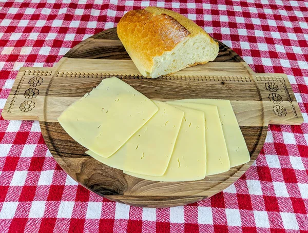 Пикник с красочной красной скатертью и деревянной доской с домашним хлебом и ломтиками сыра — стоковое фото