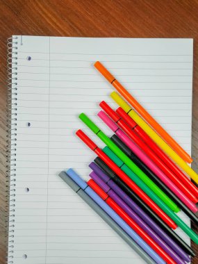 Üzerinde satır, delik ve spiral ve renkli kalemler olan boş beyaz defter ders notları ve daha iyi bir organizasyon almak ve okumak ve yazmak için