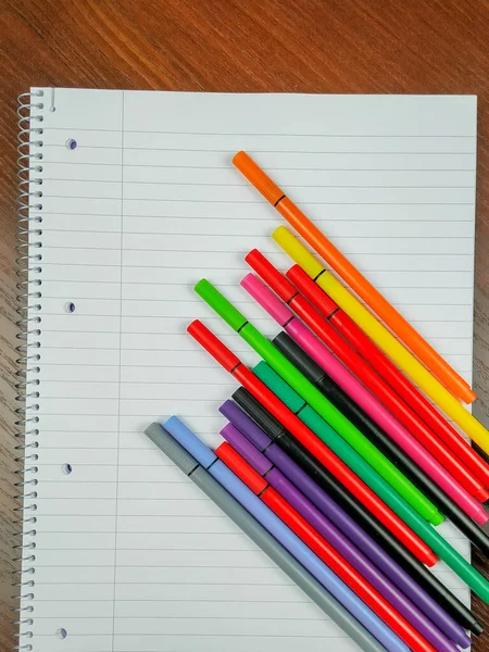 Üzerinde satır, delik ve spiral ve renkli kalemler olan boş beyaz defter ders notları ve daha iyi bir organizasyon almak ve okumak ve yazmak için