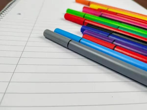 Primer plano de muchos bolígrafos con diferentes colores colocados en la parte superior del cuaderno vacío blanco con líneas para una mejor toma de notas en la escuela y una mejor organización — Foto de Stock