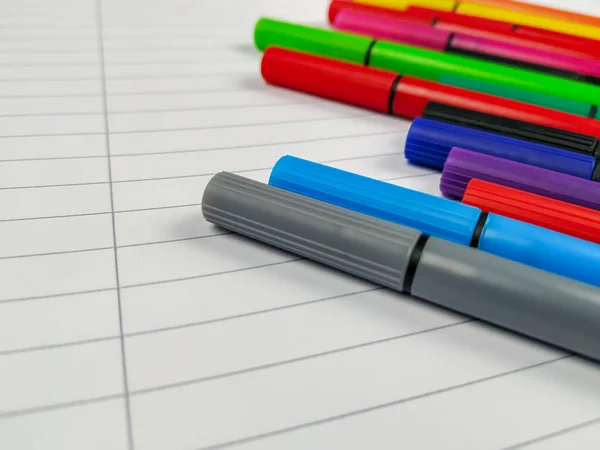 Closeup of many pens with different colors laying on the top of the white empty notebook with lines for better note taking and fun learning — Stock Photo, Image