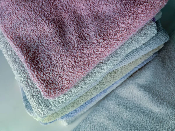 Toalhas limpas dobradas e empilhadas umas nas outras, feitas de tecido macio de algodão em cores diferentes para absorver umidade e cuidados básicos de higiene — Fotografia de Stock